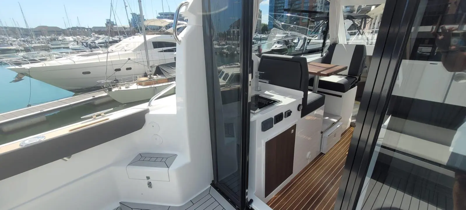 A view of a modern yacht's interior, showcasing seating, a small kitchenette, and a marina filled with moored boats.